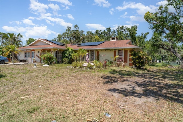 ranch-style house with stucco siding, a front yard, and solar panels