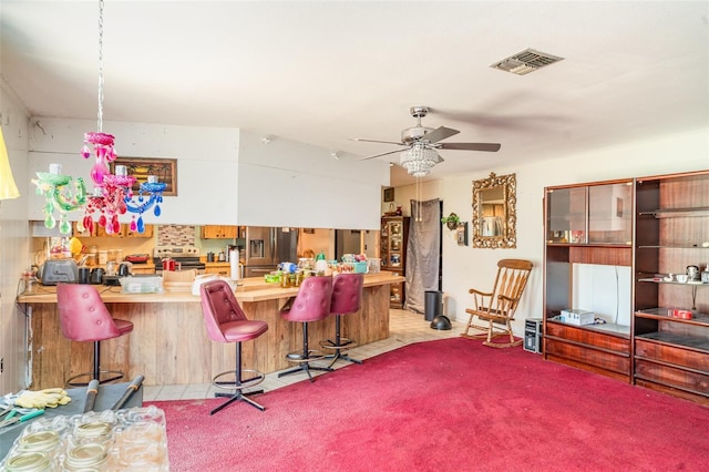 interior space with ceiling fan, a breakfast bar, light countertops, a peninsula, and visible vents