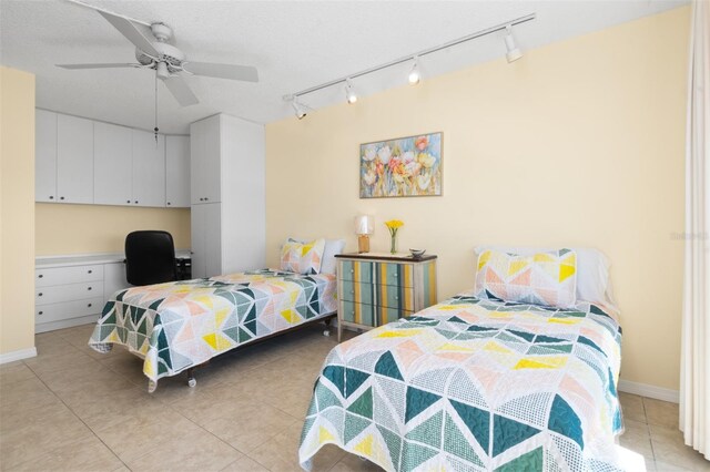 bedroom featuring light tile patterned flooring, built in study area, rail lighting, and ceiling fan