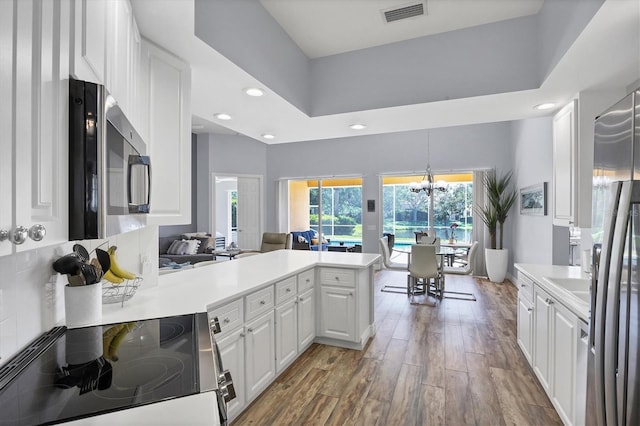 5881 Girona Pl, Sarasota, FL 34238 - kitchen with stainless steel appliances, a peninsula, white cabinets, wood finished floors, and recessed lighting