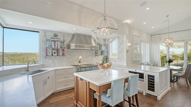 kitchen with a sink, backsplash, a chandelier, lofted ceiling, and wall chimney range hood