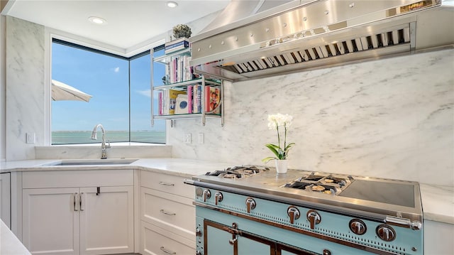 kitchen featuring white cabinets, stainless steel gas stovetop, exhaust hood, and a sink