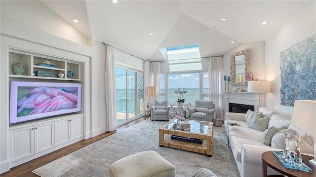 living area featuring a water view, a glass covered fireplace, recessed lighting, lofted ceiling, and wood finished floors