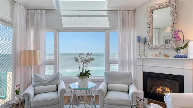 sitting room with a glass covered fireplace, wood finished floors, and a water view