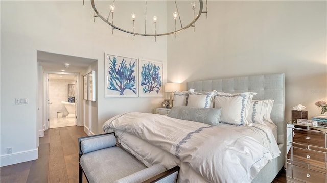 bedroom featuring connected bathroom, baseboards, a towering ceiling, and wood finished floors