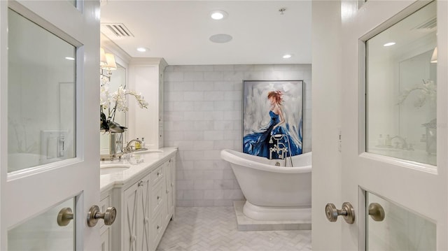 bathroom featuring tile patterned floors, double vanity, visible vents, tile walls, and a soaking tub