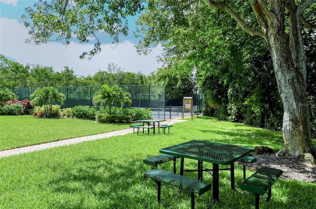 view of community featuring fence, a yard, and a tennis court