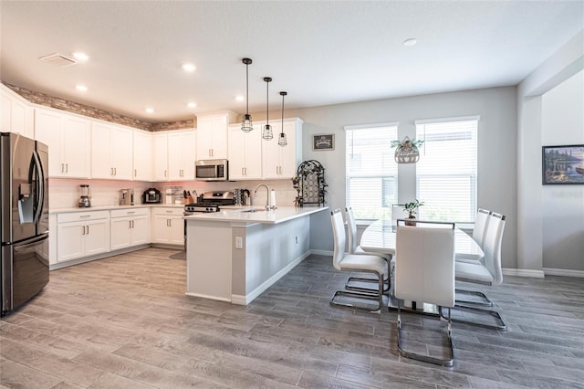 kitchen with a peninsula, appliances with stainless steel finishes, wood finished floors, and a sink
