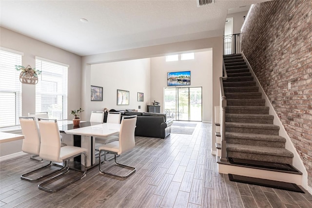 dining space featuring brick wall, baseboards, wood finished floors, and stairs