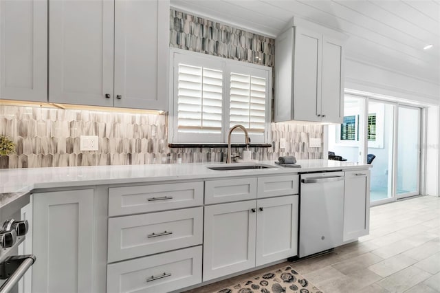 kitchen with stainless steel dishwasher, a sink, light countertops, backsplash, and white cabinetry