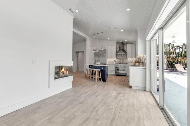 kitchen with premium appliances, wall chimney range hood, light countertops, a kitchen bar, and light wood-style flooring