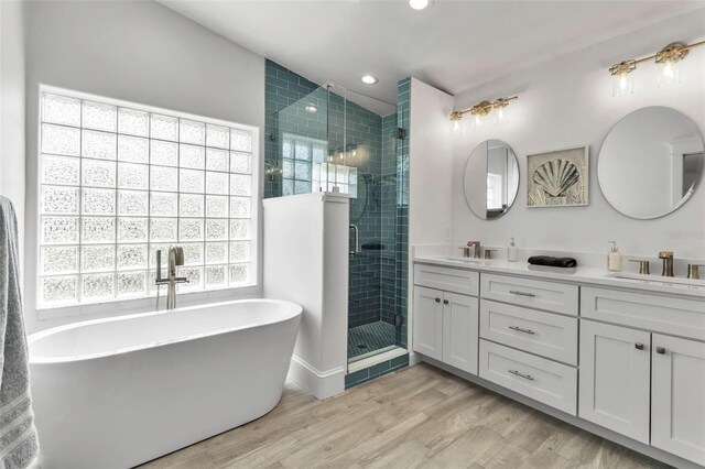 bathroom featuring a stall shower, wood finished floors, double vanity, and a sink
