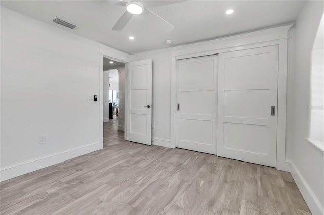 unfurnished bedroom featuring visible vents, arched walkways, a closet, baseboards, and light wood-style flooring