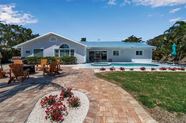 back of house featuring metal roof, a patio area, a lawn, and stucco siding