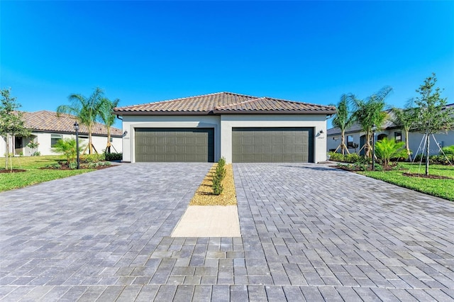 mediterranean / spanish-style house featuring stucco siding, decorative driveway, a front lawn, an attached garage, and a tile roof