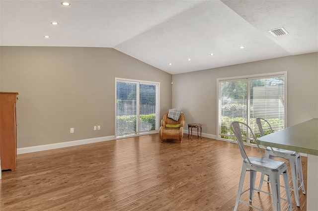living area featuring lofted ceiling, wood finished floors, visible vents, and baseboards