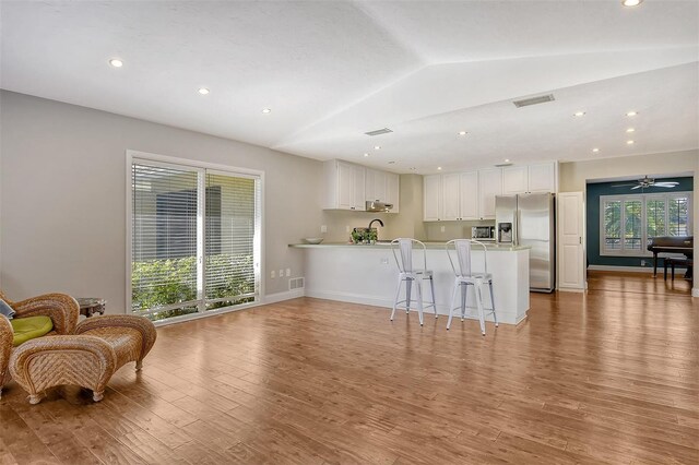 kitchen with stainless steel appliances, a peninsula, light wood-style floors, lofted ceiling, and light countertops