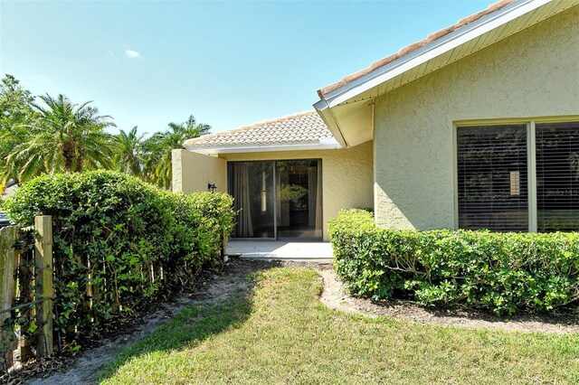 view of exterior entry with a tile roof, a yard, and stucco siding