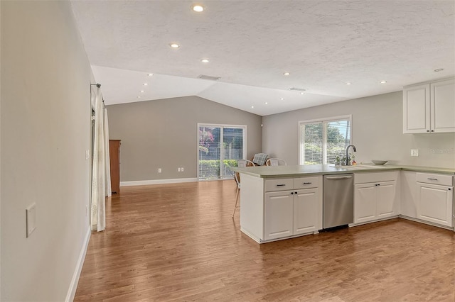 kitchen with white cabinets, a peninsula, stainless steel dishwasher, light wood finished floors, and vaulted ceiling
