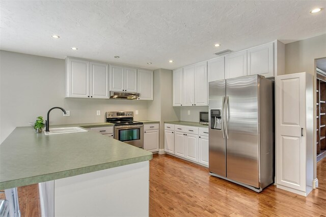 kitchen with stainless steel appliances, a peninsula, a sink, light wood-style floors, and under cabinet range hood