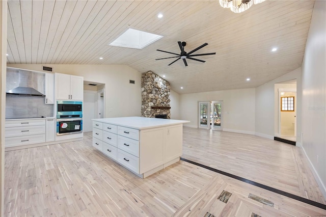 4916 Hidden Oaks Trl, Sarasota, FL 34232 - kitchen with wall chimney range hood, lofted ceiling, light wood-style floors, a skylight, and white cabinetry