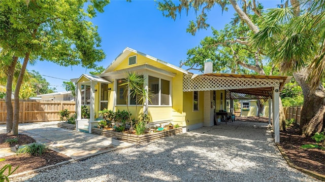 bungalow-style house featuring fence, driveway, a chimney, and an attached carport