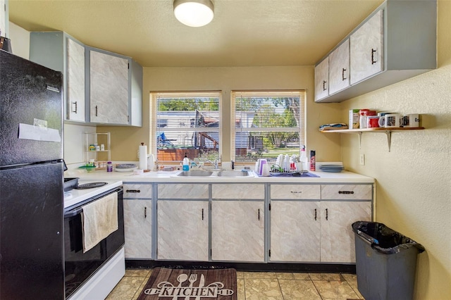 kitchen featuring open shelves, electric stove, a sink, light countertops, and freestanding refrigerator
