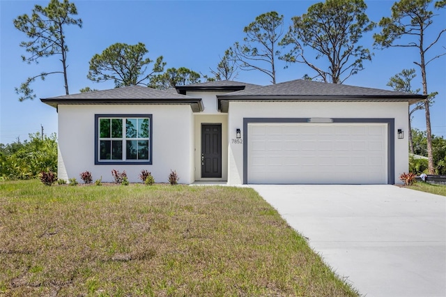 prairie-style home featuring a garage, concrete driveway, a front lawn, and stucco siding