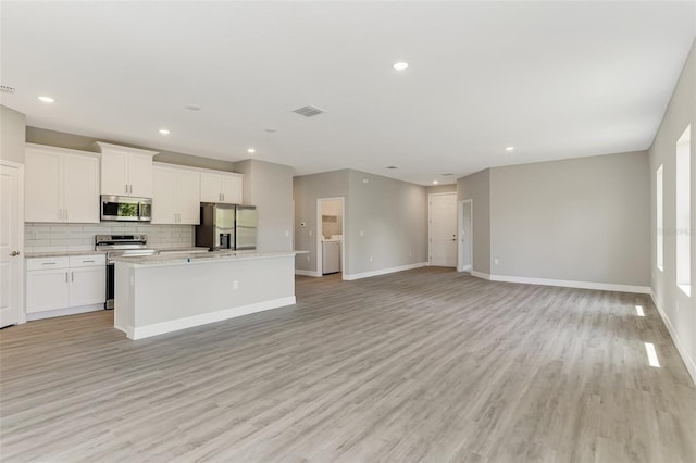 kitchen with stainless steel appliances, light wood-style flooring, baseboards, decorative backsplash, and a kitchen island