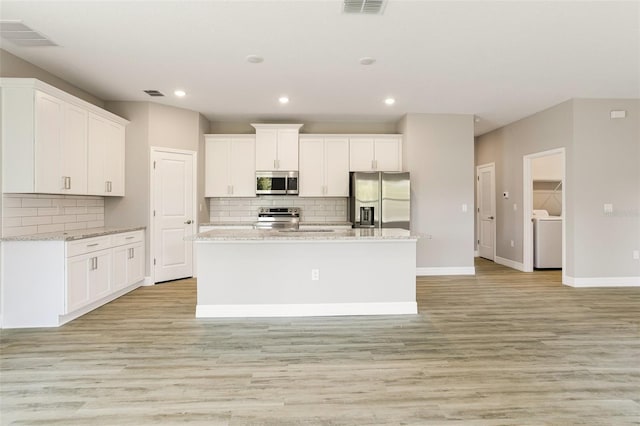 kitchen featuring tasteful backsplash, white cabinetry, a center island with sink, and stainless steel appliances