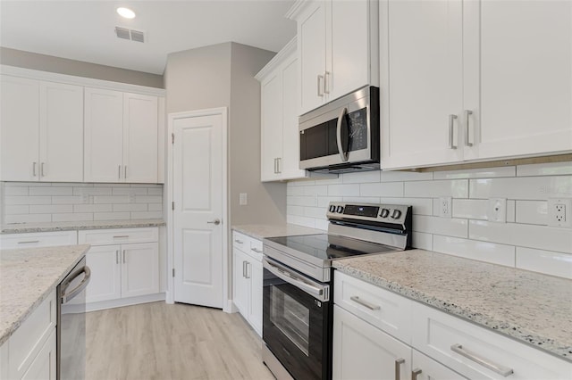 kitchen with white cabinets, stainless steel appliances, visible vents, and decorative backsplash