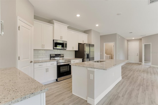 kitchen with a kitchen island with sink, stainless steel appliances, light wood-style flooring, backsplash, and visible vents