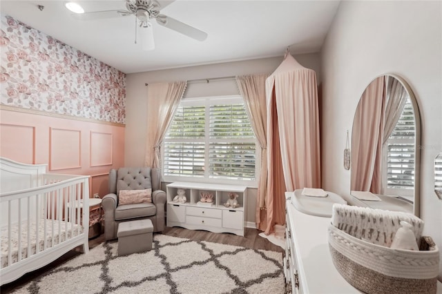 5023 Brickell Park Cv, Bradenton, FL 34211 - bedroom with a wainscoted wall, a crib, wallpapered walls, wood finished floors, and ceiling fan