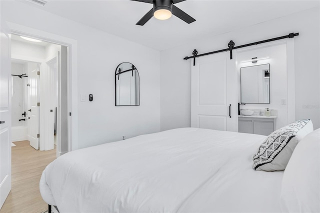 1921 Fern Ave, Sarasota, FL 34235 - bedroom featuring connected bathroom, light wood-type flooring, a barn door, and ceiling fan