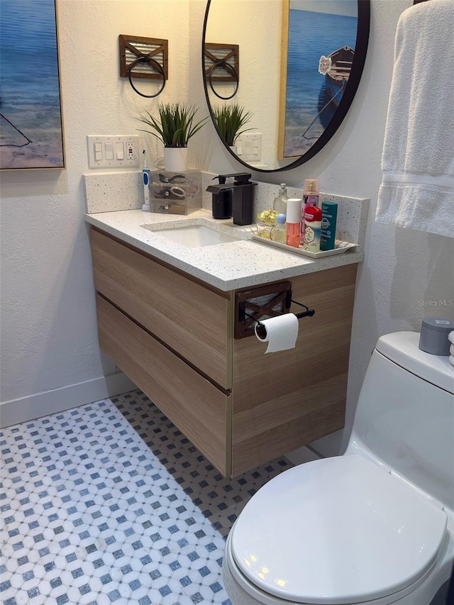 bathroom featuring a textured wall, toilet, vanity, and baseboards