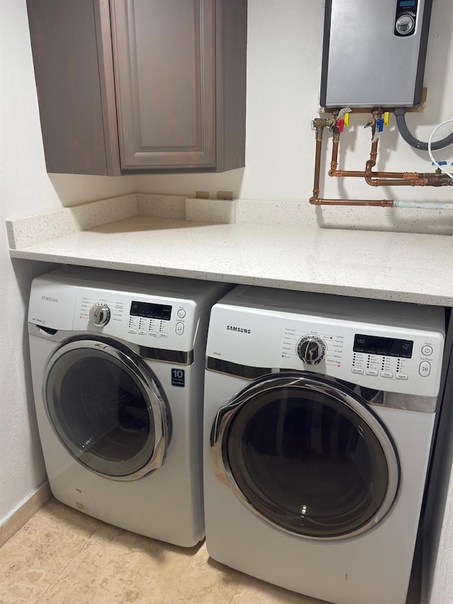 clothes washing area with water heater, washing machine and dryer, baseboards, and cabinet space