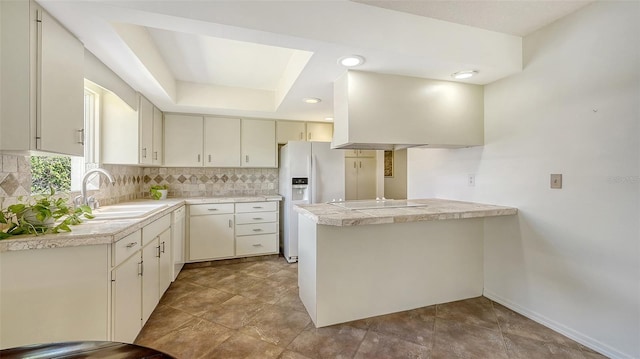 kitchen featuring tasteful backsplash, black electric stovetop, a sink, white refrigerator with ice dispenser, and a tray ceiling