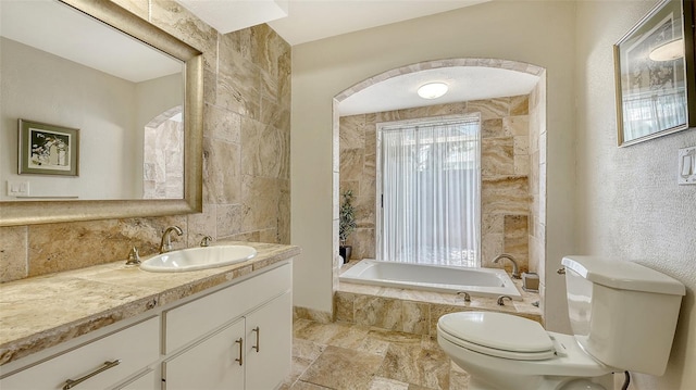 full bath with decorative backsplash, vanity, stone finish flooring, toilet, and tiled tub