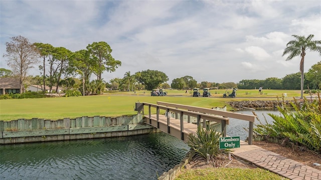 view of dock with golf course view, a water view, and a lawn
