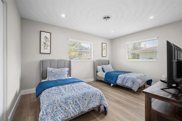 bedroom featuring visible vents, baseboards, wood finished floors, and multiple windows