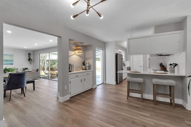 kitchen featuring freestanding refrigerator, a peninsula, light countertops, white cabinetry, and light wood finished floors
