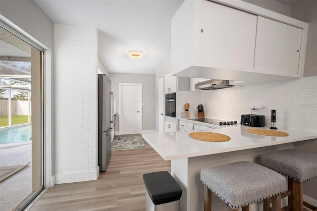 kitchen with a peninsula, a kitchen bar, light wood-type flooring, backsplash, and black appliances