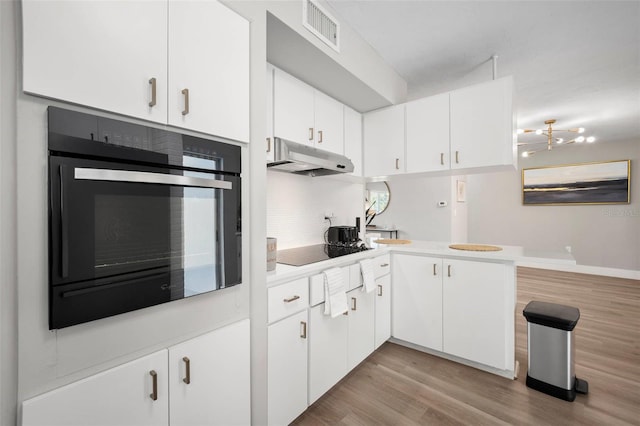 kitchen featuring visible vents, light countertops, under cabinet range hood, white cabinets, and black appliances