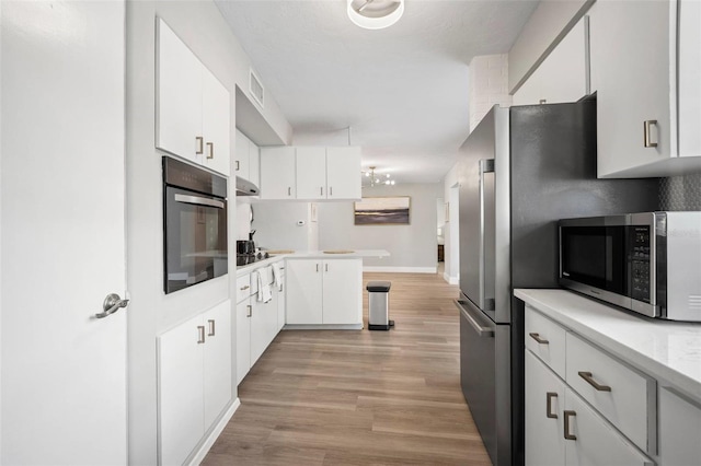 kitchen featuring light countertops, stainless steel microwave, light wood-style floors, black oven, and white cabinetry
