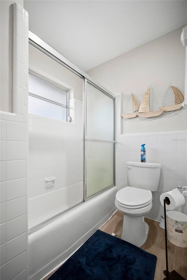 full bath with shower / bath combination with glass door, wood finished floors, toilet, and a wainscoted wall