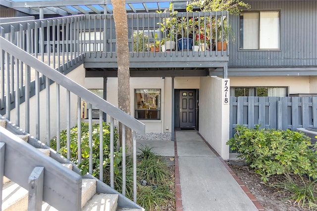doorway to property with stucco siding, fence, and a balcony