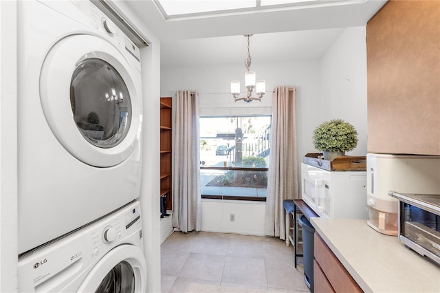 laundry area featuring a notable chandelier, light tile patterned floors, stacked washer / dryer, and laundry area