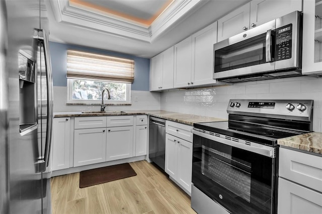 kitchen with stainless steel appliances, a sink, a tray ceiling, and white cabinets