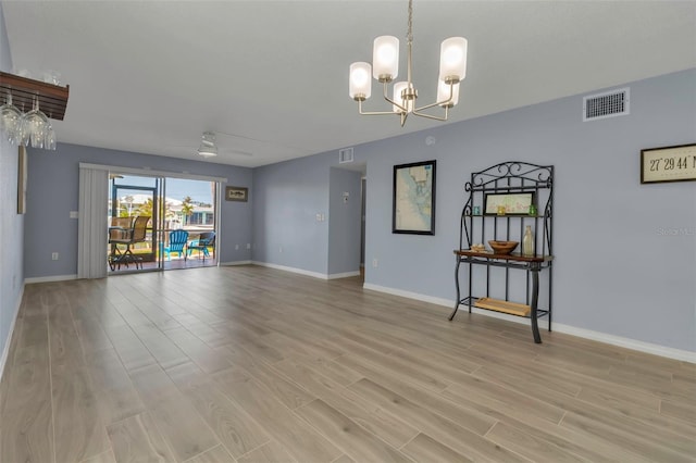spare room featuring light wood finished floors, a chandelier, and baseboards