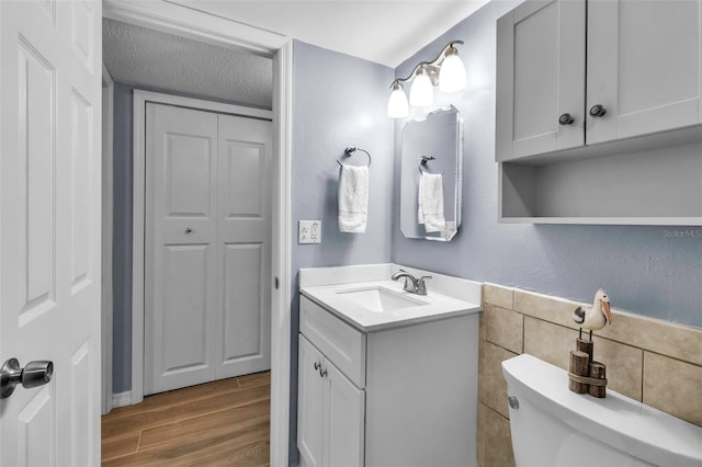 bathroom featuring toilet, wood finished floors, tile walls, vanity, and a textured ceiling